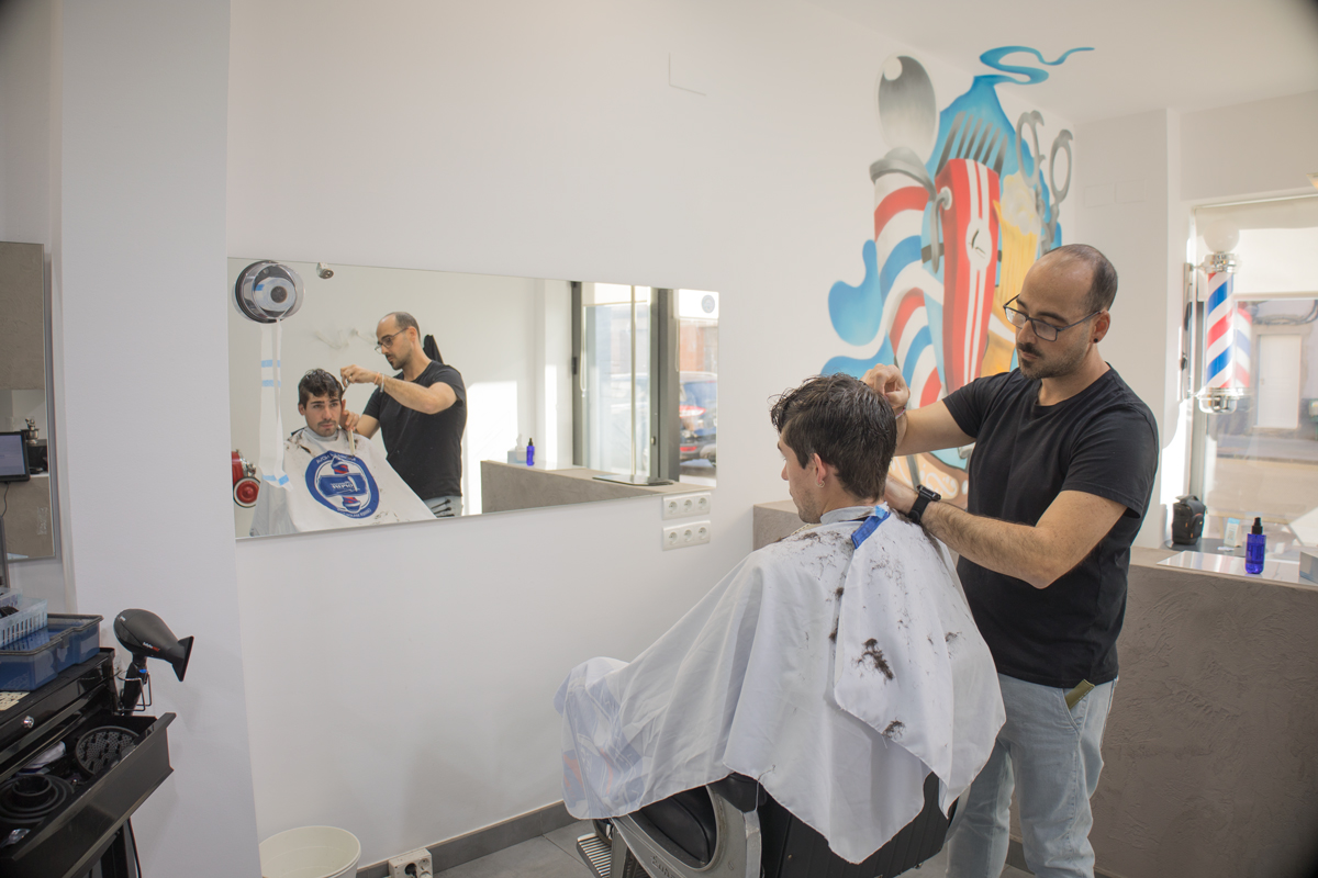 Fotografía del interior de la peluquería donde se ve el peluquero que está cortándole el pelo a un muchacho.